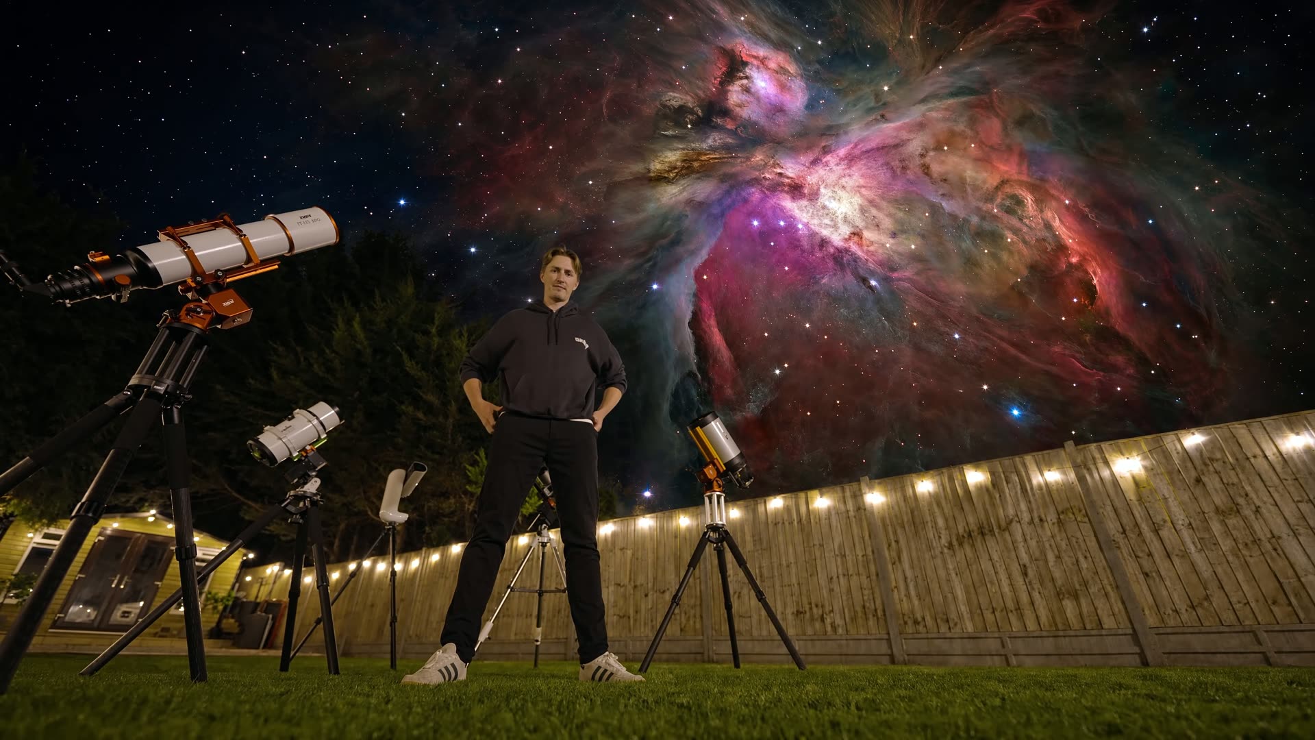 Damon Scotting standing among telescopes in his garden, a nebula filling the night sky